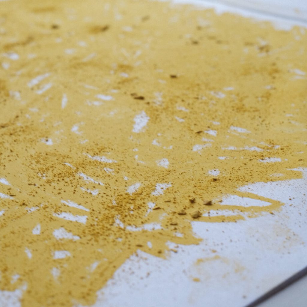 A close up of the paper painted with the yellow soft pastel, showing the dust and bits of the broken stick.