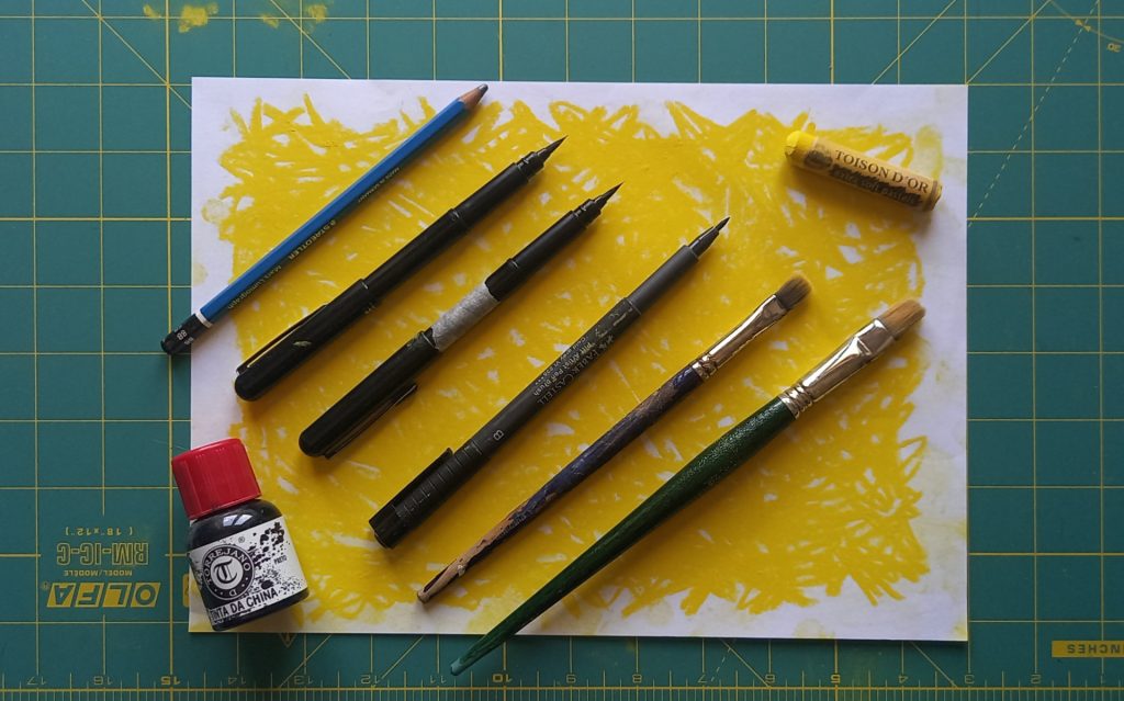 Drawing tools on the table - a softlead pencil, ink pens, brushes, a bottle of drawing ink and a soft pastel stick.